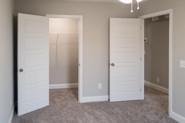 unfurnished bedroom featuring a closet, a walk in closet, baseboards, and carpet floors