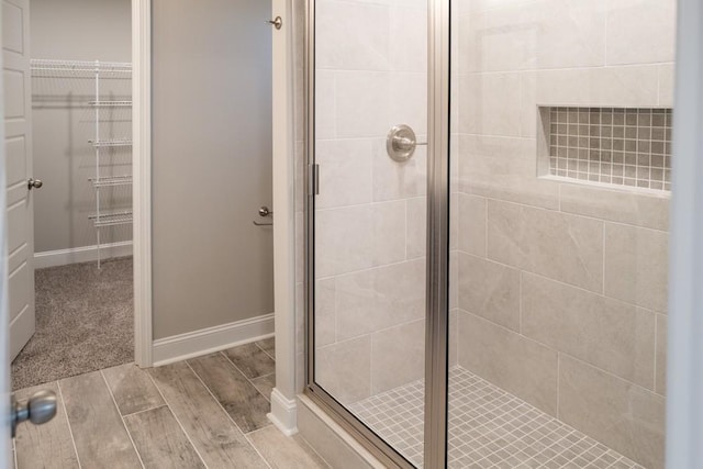 full bath featuring wood finish floors, a walk in closet, baseboards, and a shower stall