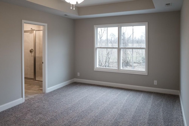 unfurnished room with a tray ceiling, carpet flooring, baseboards, and visible vents