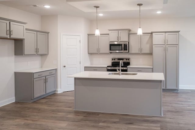 kitchen featuring a kitchen island with sink, dark wood-style flooring, gray cabinets, appliances with stainless steel finishes, and decorative light fixtures