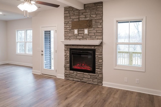 unfurnished living room featuring beamed ceiling, a ceiling fan, wood finished floors, a fireplace, and baseboards