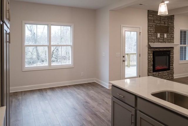 kitchen featuring wood finished floors, baseboards, gray cabinets, a stone fireplace, and open floor plan