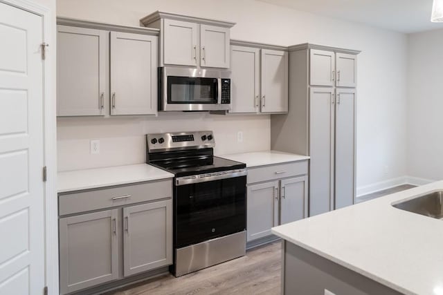 kitchen featuring light wood-style flooring, appliances with stainless steel finishes, light countertops, and gray cabinetry