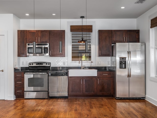 kitchen featuring dark countertops, tasteful backsplash, dark wood-type flooring, stainless steel appliances, and a sink