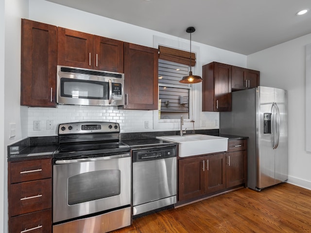 kitchen featuring a sink, dark wood-type flooring, appliances with stainless steel finishes, dark countertops, and decorative light fixtures