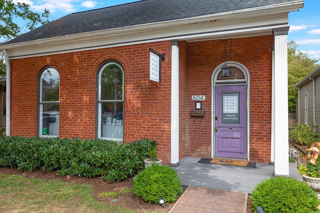 view of exterior entry featuring brick siding and roof with shingles