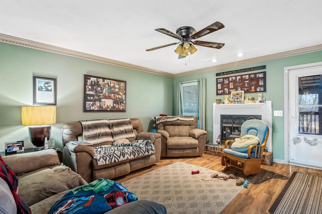 living room with wood finished floors, baseboards, a fireplace with raised hearth, ceiling fan, and ornamental molding