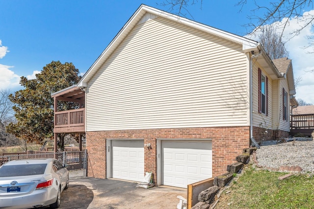 view of side of home with driveway, a balcony, fence, a garage, and brick siding