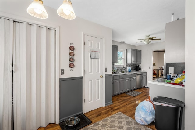 kitchen featuring gray cabinetry, light countertops, stainless steel dishwasher, dark wood-style floors, and a sink