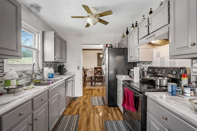 kitchen with under cabinet range hood, light wood-type flooring, gray cabinets, appliances with stainless steel finishes, and a sink