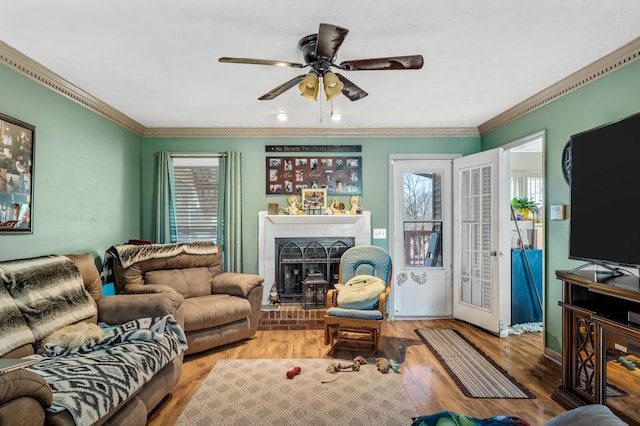 living room with a ceiling fan, a brick fireplace, wood finished floors, and crown molding