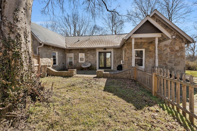 rear view of property with fence, french doors, metal roof, stone siding, and a patio