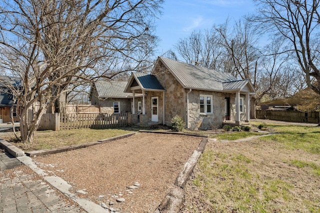 view of front of home with a front yard, fence, a standing seam roof, stone siding, and metal roof