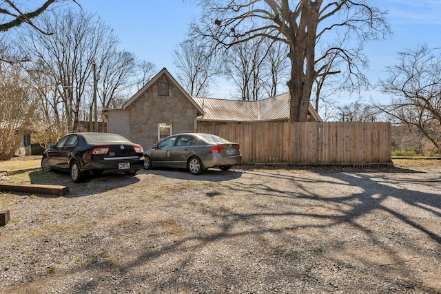 view of property exterior featuring metal roof, stone siding, and fence