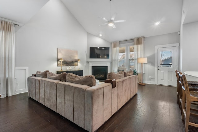 living area featuring dark wood finished floors, a glass covered fireplace, a ceiling fan, and high vaulted ceiling