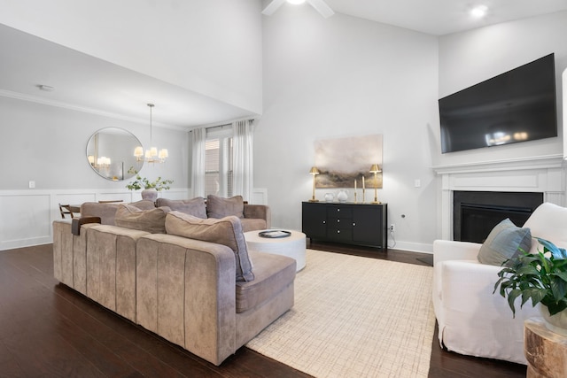 living room featuring a fireplace, dark wood-style flooring, wainscoting, crown molding, and a chandelier