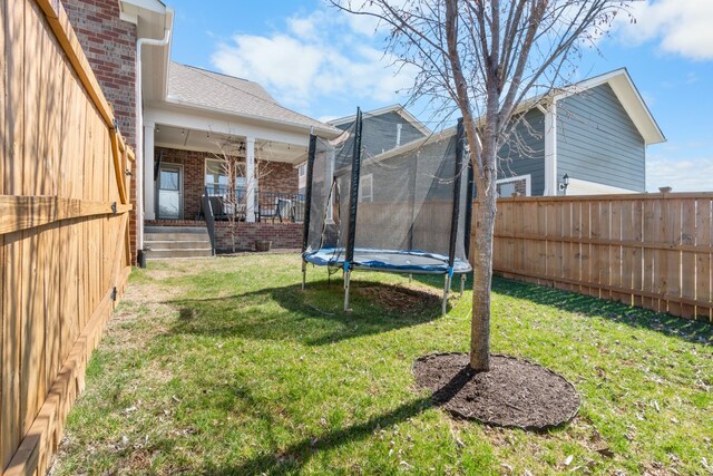 view of yard with ceiling fan, a trampoline, and fence