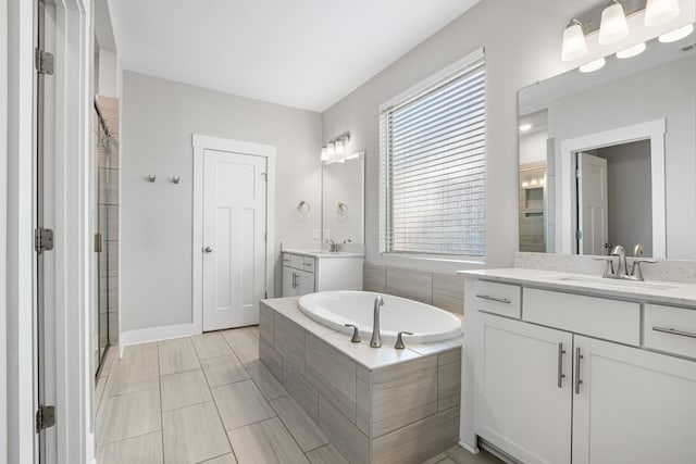 full bathroom with a stall shower, two vanities, a garden tub, and a sink