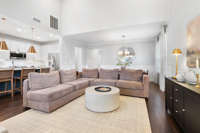 living area with visible vents, crown molding, dark wood finished floors, a wainscoted wall, and a notable chandelier