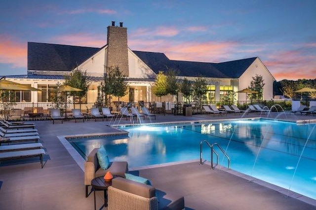 pool at dusk with a patio, a community pool, and fence