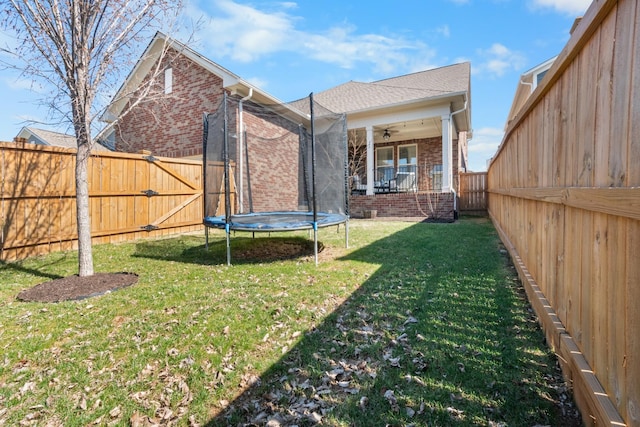 view of yard featuring a fenced backyard, a ceiling fan, a trampoline, and a gate