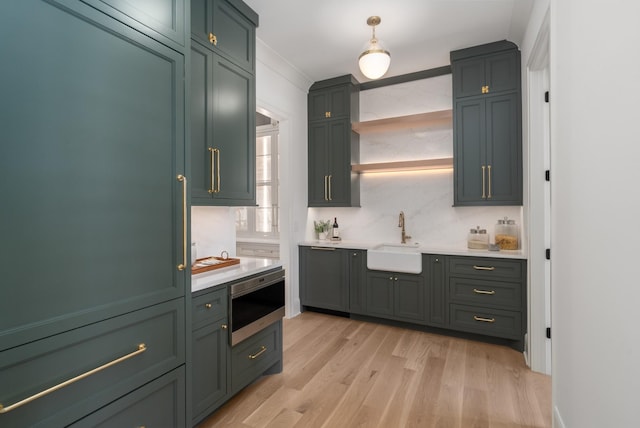 kitchen with stainless steel microwave, a sink, light countertops, light wood-style floors, and green cabinetry