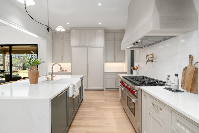 kitchen featuring light wood finished floors, range with two ovens, recessed lighting, a sink, and custom range hood