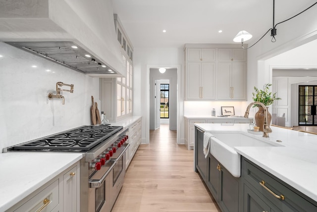 kitchen featuring double oven range, light countertops, custom range hood, and a sink