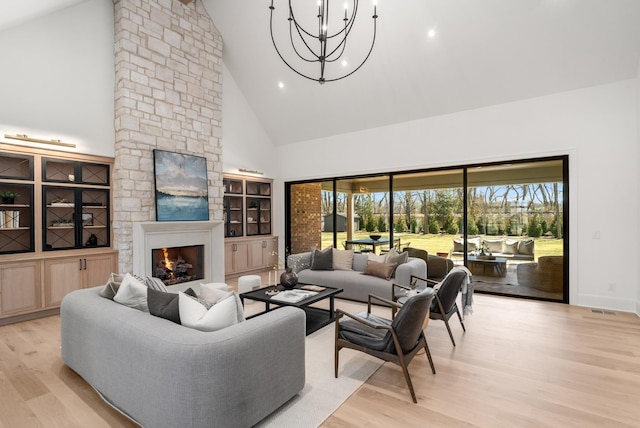 living area with light wood-type flooring, high vaulted ceiling, an inviting chandelier, a fireplace, and baseboards