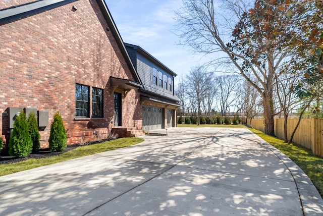 view of side of property featuring brick siding, concrete driveway, an attached garage, and fence