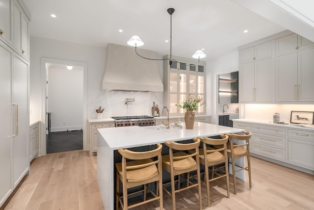 kitchen featuring light wood finished floors, a center island with sink, light countertops, and custom range hood