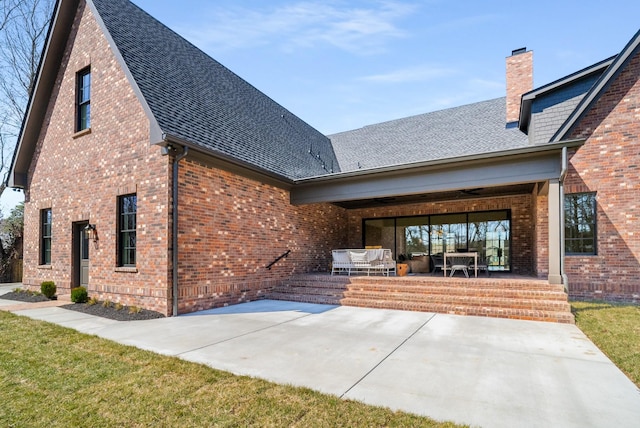 rear view of house with roof with shingles, an outdoor living space, a chimney, a patio area, and brick siding