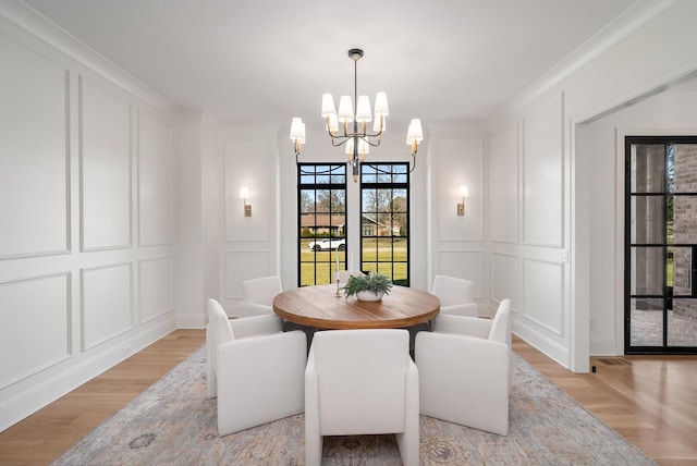 dining area featuring a decorative wall, ornamental molding, light wood-type flooring, and a chandelier