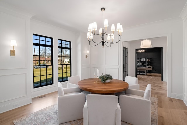 dining area featuring light wood-style floors, a decorative wall, crown molding, and visible vents