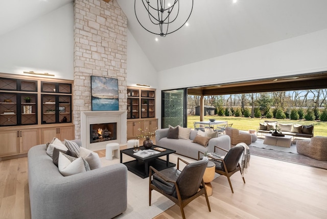 living area with a stone fireplace, an inviting chandelier, light wood-style flooring, and high vaulted ceiling