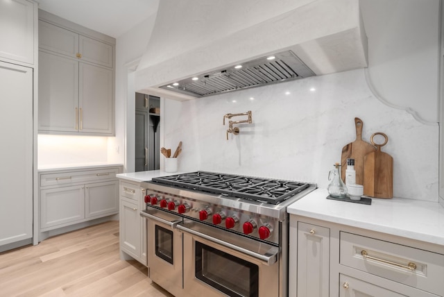 kitchen with backsplash, double oven range, light countertops, light wood-type flooring, and custom range hood