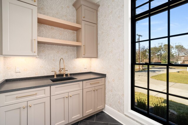 kitchen featuring dark countertops, wallpapered walls, baseboards, and a sink