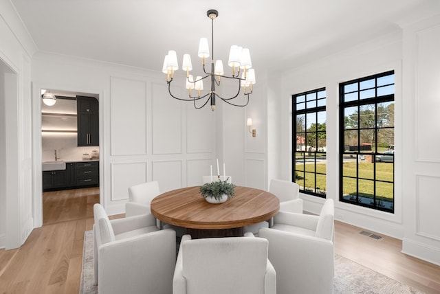 dining space with a decorative wall, light wood-style flooring, crown molding, and visible vents