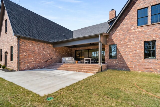 rear view of house with brick siding, a shingled roof, a chimney, a patio area, and a ceiling fan