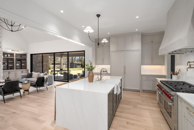 kitchen with light wood-style flooring, custom range hood, a sink, light countertops, and range with two ovens