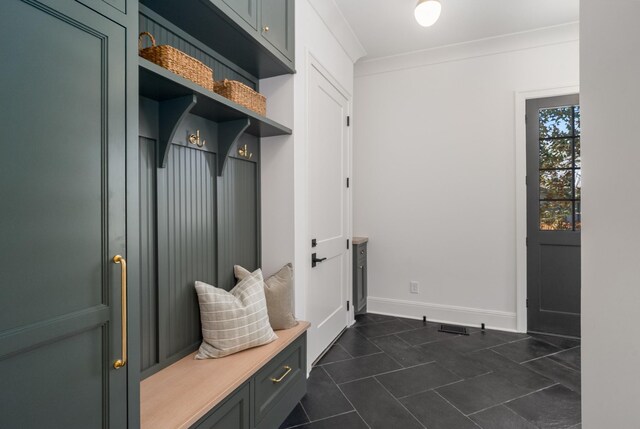 mudroom with crown molding, dark tile patterned floors, and baseboards