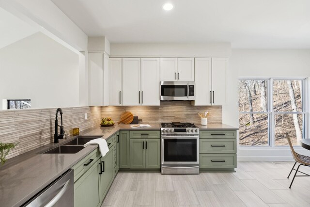 kitchen featuring green cabinetry, decorative backsplash, appliances with stainless steel finishes, and a sink