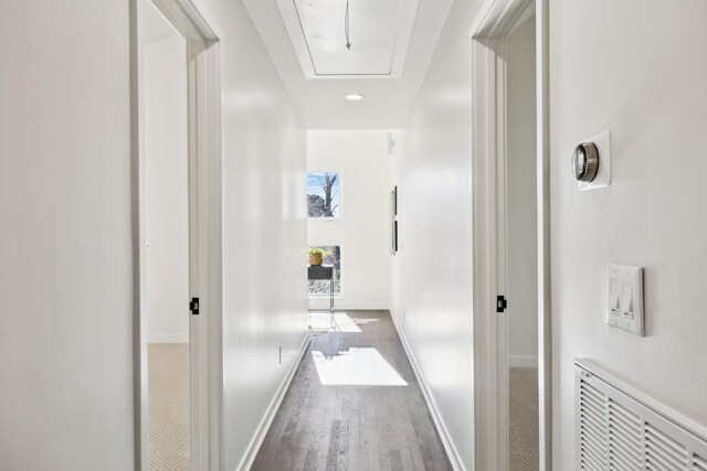 corridor featuring visible vents, baseboards, attic access, and wood finished floors