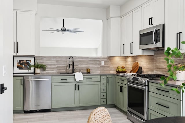 kitchen featuring green cabinetry, a sink, stainless steel appliances, dark countertops, and tasteful backsplash