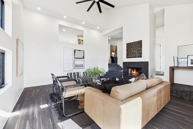 living room featuring baseboards, recessed lighting, a warm lit fireplace, wood finished floors, and high vaulted ceiling