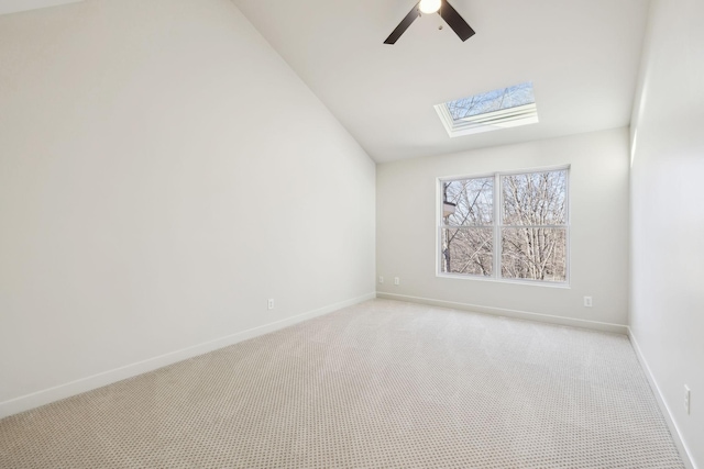 spare room with lofted ceiling with skylight, light colored carpet, baseboards, and ceiling fan