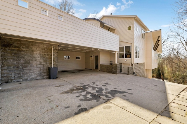 back of property with a carport, stone siding, and concrete driveway