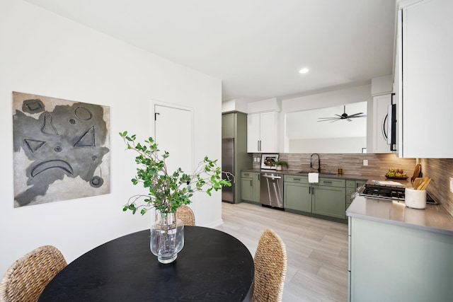 kitchen with a sink, backsplash, appliances with stainless steel finishes, green cabinetry, and ceiling fan