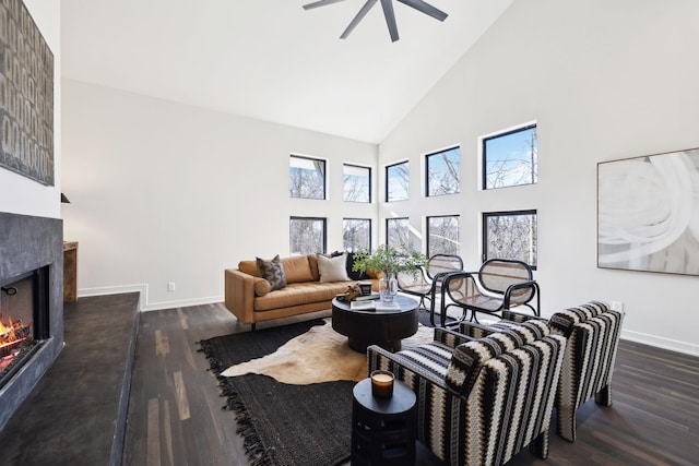 living area featuring baseboards, a warm lit fireplace, and wood finished floors