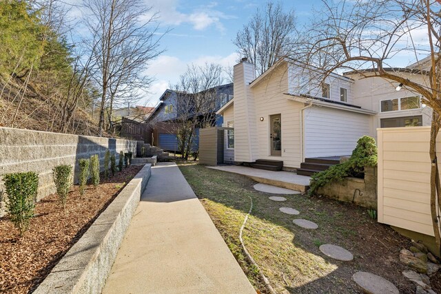 view of property exterior featuring entry steps, a chimney, and fence